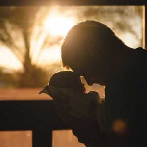 silhouette of father holding newborn baby close to his face with setting sun in background