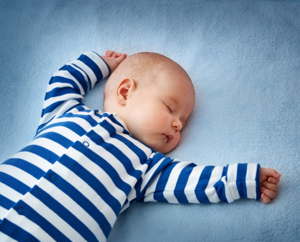 Baby in blue and white striped pajamas sleeping on his back with head turned